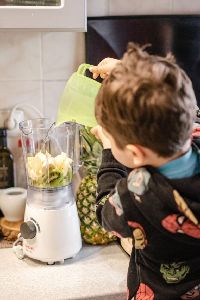Leinsamen im Smoothie verwenden: Kind gießt Wasser zu Obst im Mixer