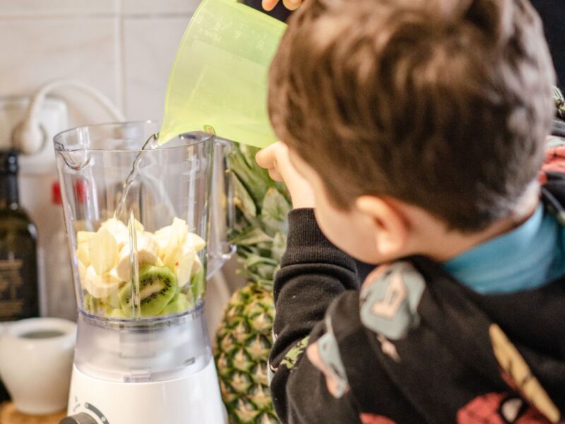 Leinsamen im Smoothie verwenden: Kind gießt Wasser zu Obst im Mixer